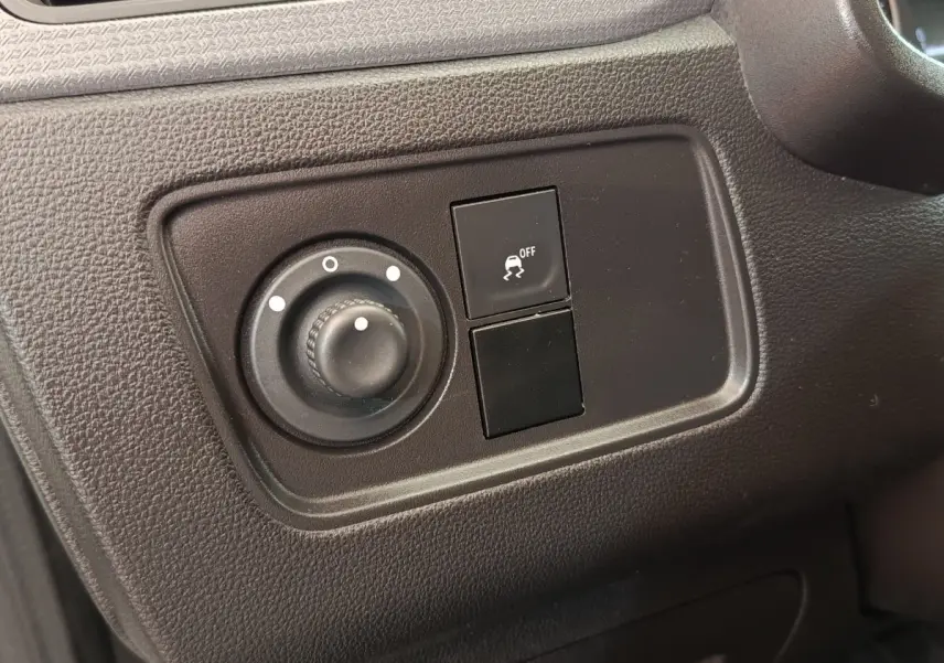 Gros plan sur les commandes de réglage des phares et de l'antipatinage dans le tableau de bord noir du Renault Express blanc.