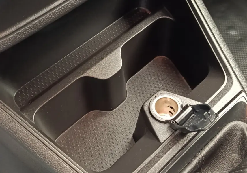 Gros plan sur la prise 12V ouverte et le rangement central noir dans l'habitacle du Renault Express blanc.
