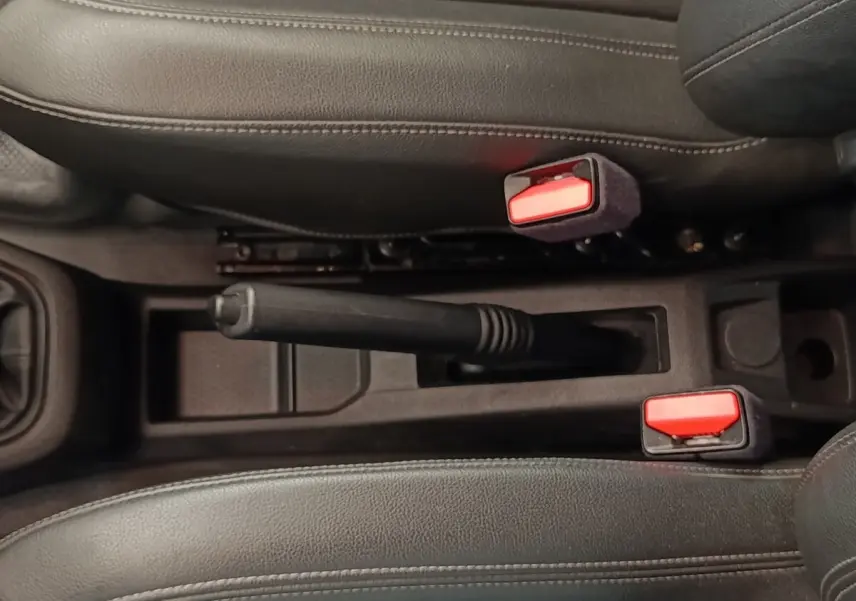 Vue rapprochée de la console centrale noire du Renault Express 2023, avec frein à main manuel et ceintures rouges.