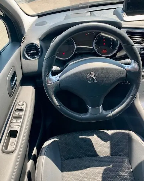 Vue intérieure du poste de conduite du Peugeot 3008 noir 2014, volant cuir avec logo lion et tableau de bord digital.