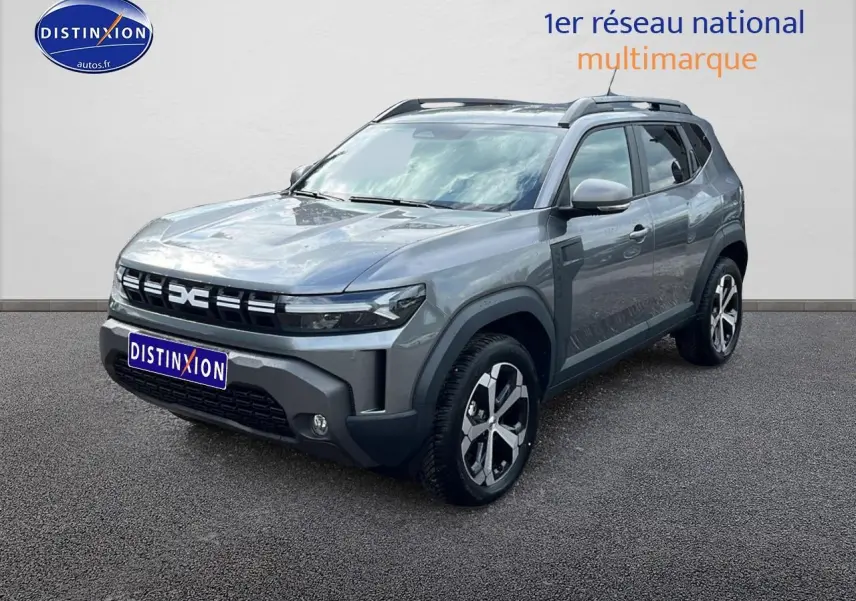 Dacia Duster gris schiste en 3/4 avant droit, avec jantes alu et barres de toit visibles.