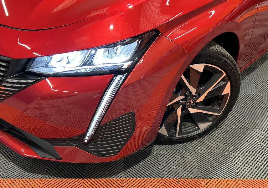 Gros plan sur l’avant droit rouge vif d’une Peugeot 308 2024 avec phare LED et jante alliage noire et argent.