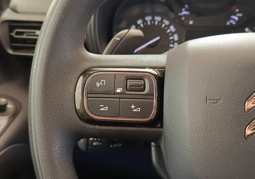 Gros plan sur le volant multifonctions noir du Citroën Berlingo blanc, avec commandes audio et téléphone visibles.
