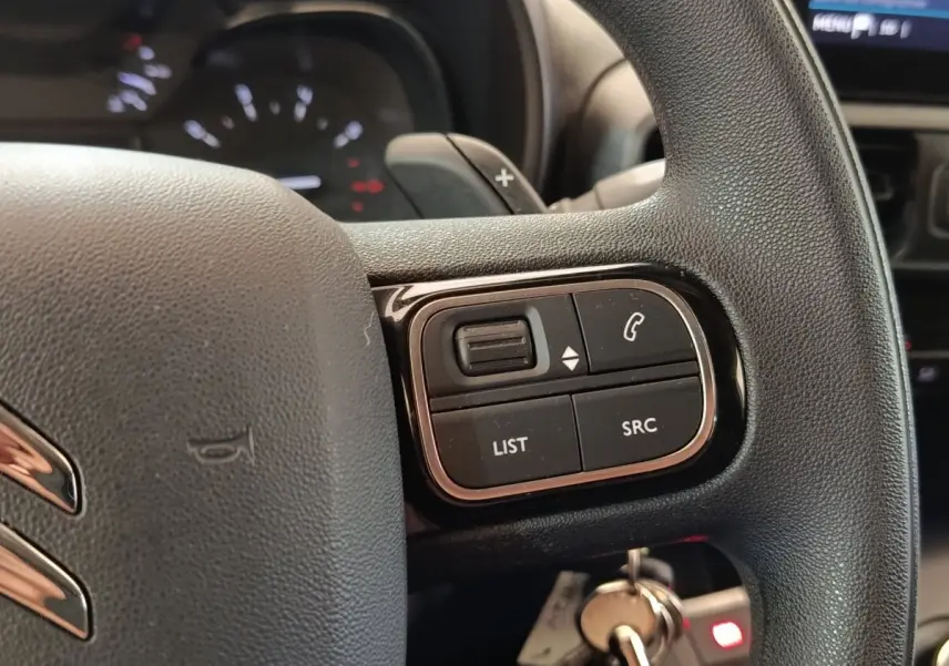 Gros plan sur le volant multifonctions noir du Citroën Berlingo blanc, avec commandes audio et téléphone visibles.
