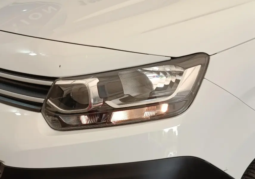 Gros plan sur le phare avant droit du Citroën Berlingo blanc, avec calandre et partie de la carrosserie visibles.