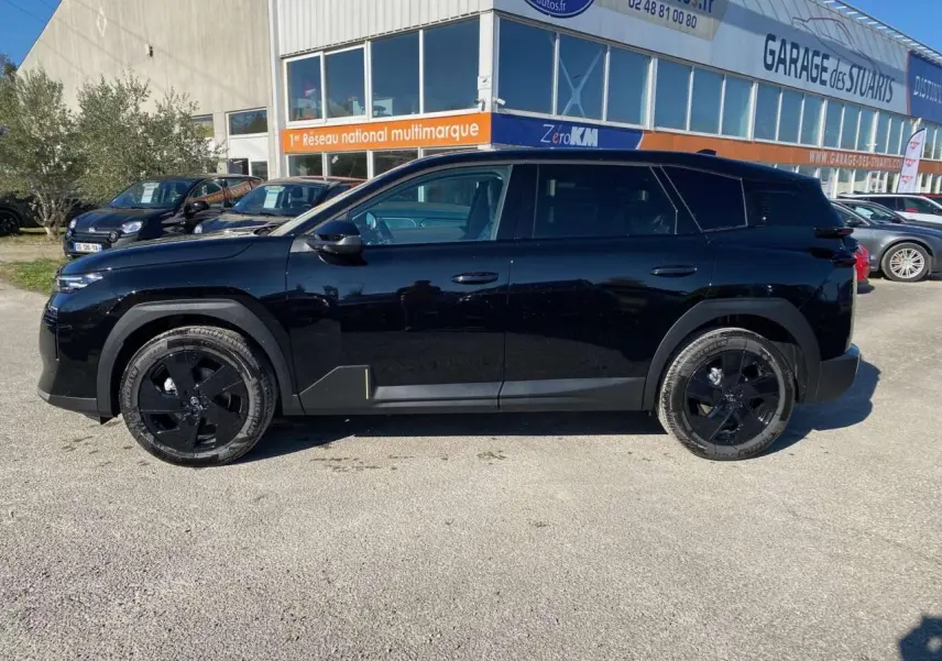 Vue de profil côté gauche d'un Citroën C5 Aircross noir avec jantes alliage noires, stationné devant un garage.