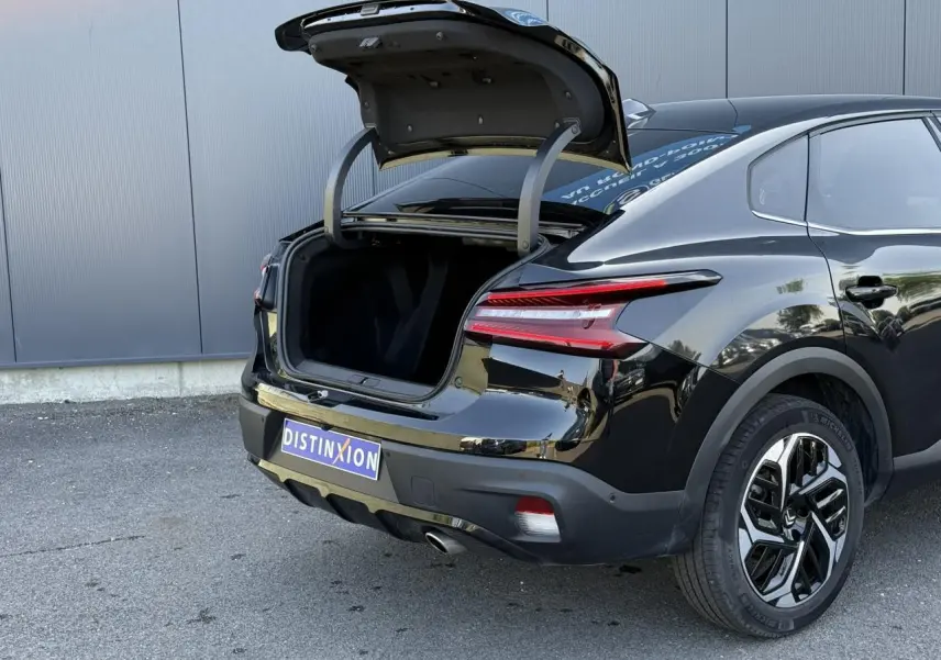 Vue 3/4 arrière droite d'une Citroën C4 X noire Perla avec coffre ouvert et jantes alliage diamantées.
