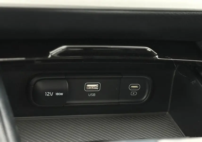 Prise USB, port USB-C et prise 12V intégrés dans la console centrale du Kia Sportage gris perle 2025.