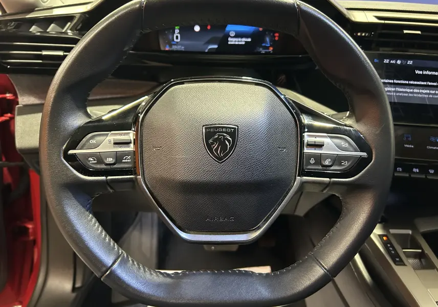 Vue rapprochée du volant cuir noir de la Peugeot 308 rouge 2024 avec commandes intégrées et tableau de bord numérique.
