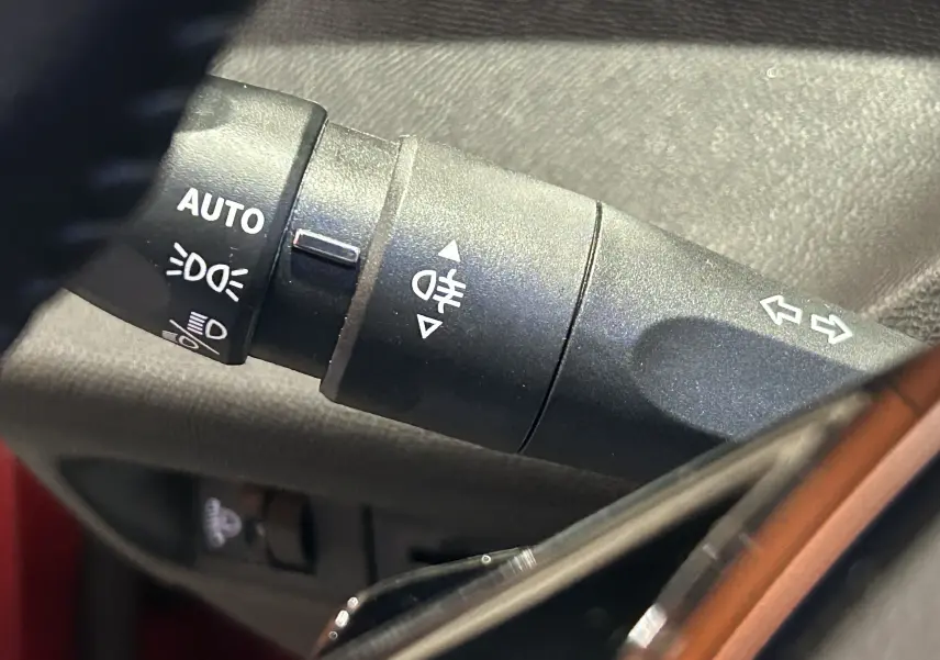 Gros plan sur la commande de phares et clignotants à gauche du volant dans le Peugeot 308 rouge 2024.