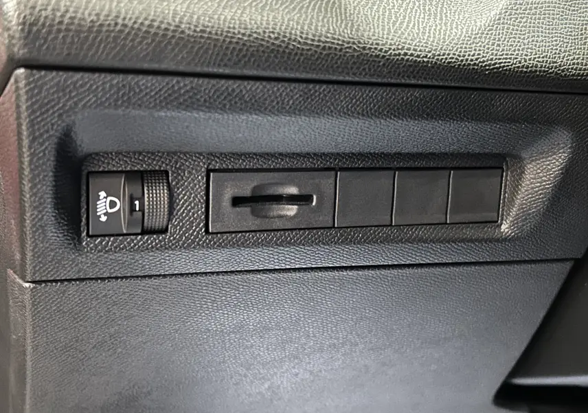 Détail du tableau de bord noir avec commande de réglage des phares sur Peugeot 308 rouge 2024.