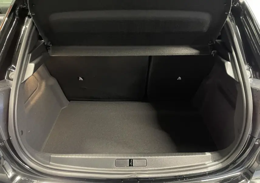 Coffre ouvert vu de l'arrière d'une Peugeot 208 noire métallisée, montrant un espace de chargement vide et propre.