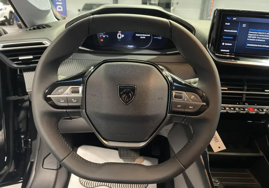 Vue rapprochée du volant cuir noir du Peugeot 208 2025 avec commandes intégrées et tableau de bord numérique.