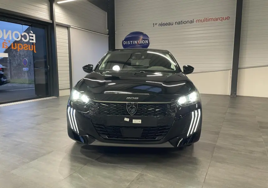 Peugeot 208 noir métallisé vue de face en intérieur, avec feux LED allumés et calandre noire brillante.