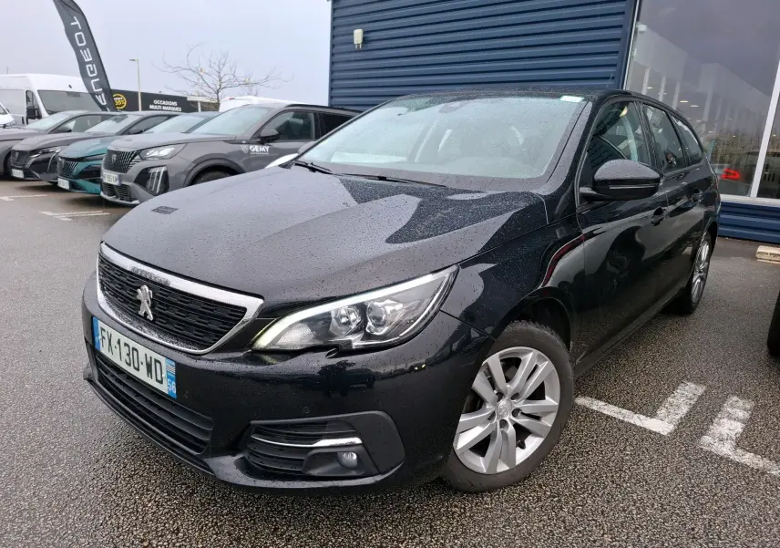 Peugeot 308 SW noire vue en 3/4 avant droit sous la pluie, avec jantes alliage et calandre chromée.