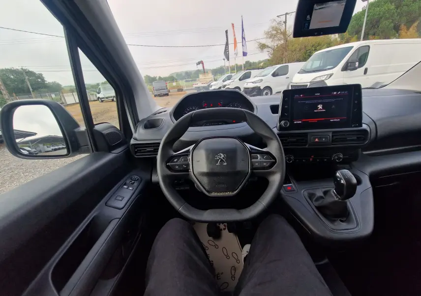 Vue intérieure centrée sur le volant et le tableau de bord du Peugeot Partner blanc, avec levier de vitesses manuel visible.