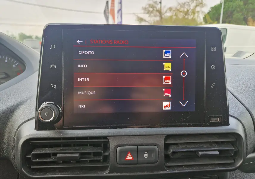 Écran tactile central du Peugeot Partner 2021 affichant la liste des stations radio, avec commandes et aérateurs visibles.