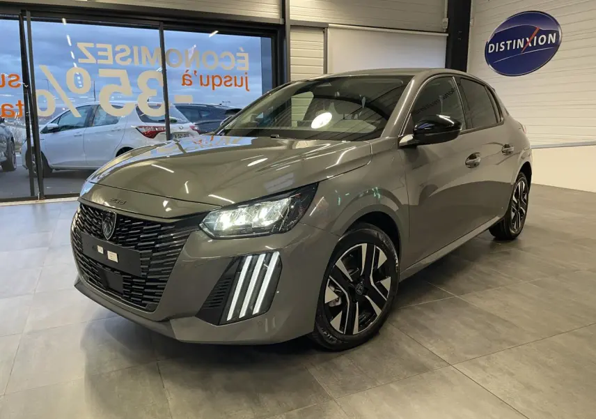 Peugeot 208 gris selenium vue 3/4 avant en intérieur, avec calandre noire et feux LED distinctifs allumés.