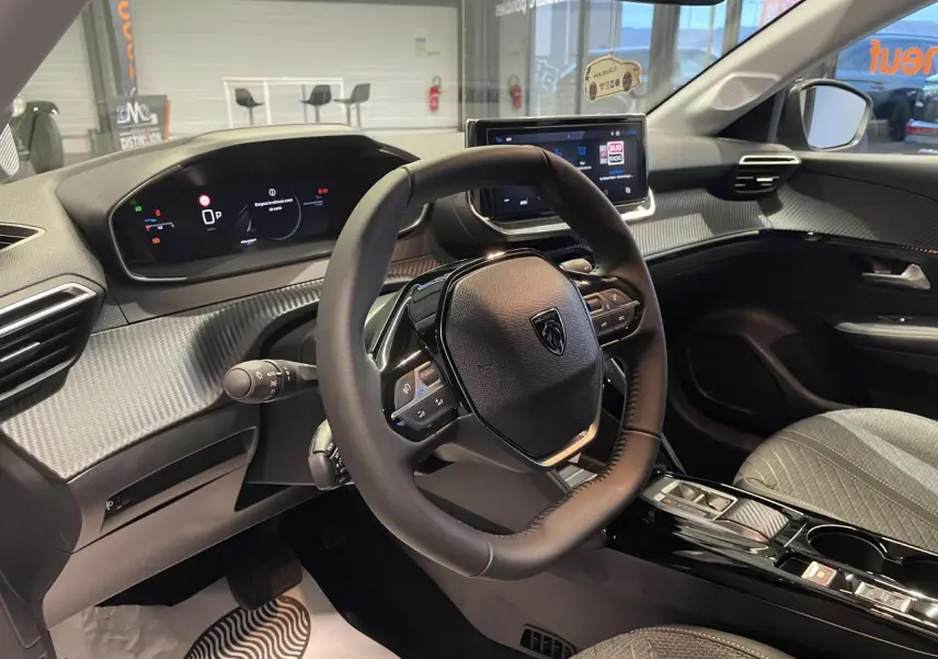 Vue intérieure de la Peugeot 208 2025 montrant le volant compact, tableau de bord numérique et console centrale noire brillante.