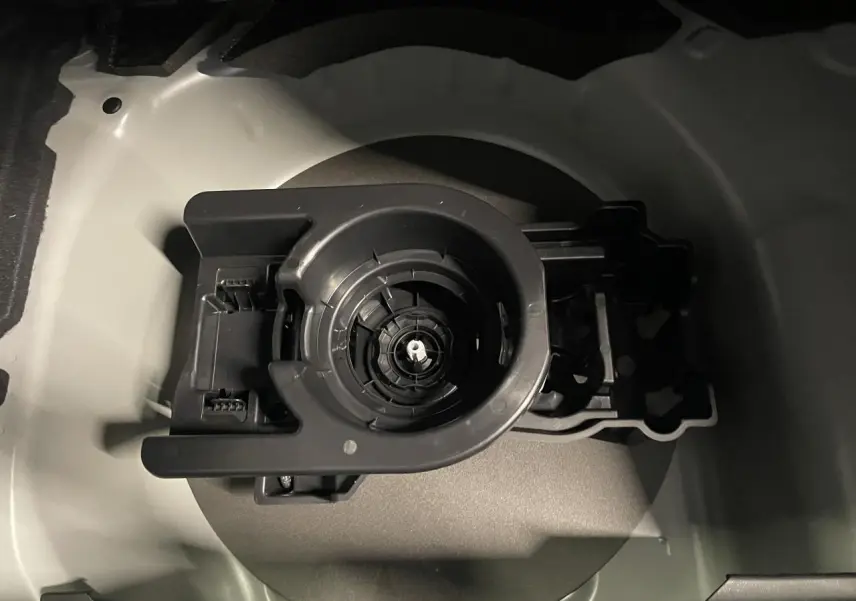 Gros plan sur le compartiment de rangement gris sélénium pour kit de dépannage pneumatique dans le coffre d'une Peugeot 208 hybride.