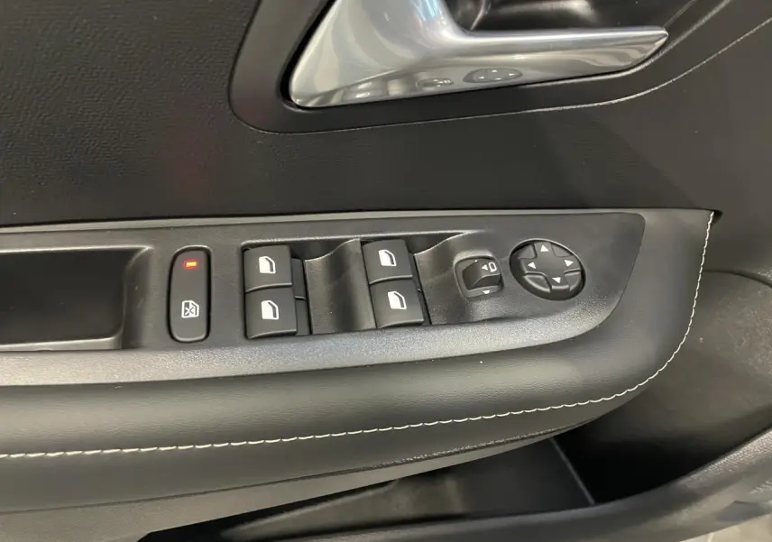 Détail des commandes de lève-vitres et réglage des rétroviseurs sur la porte avant gauche d’une Peugeot 208 gris Selenium.