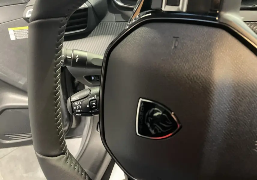 Gros plan sur le volant cuir noir de la Peugeot 208 2025 avec logo lion et commandes intégrées.