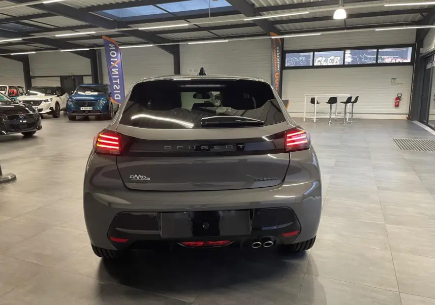Vue arrière d'une Peugeot 208 hybride gris selenium avec feux arrière allumés en intérieur showroom.