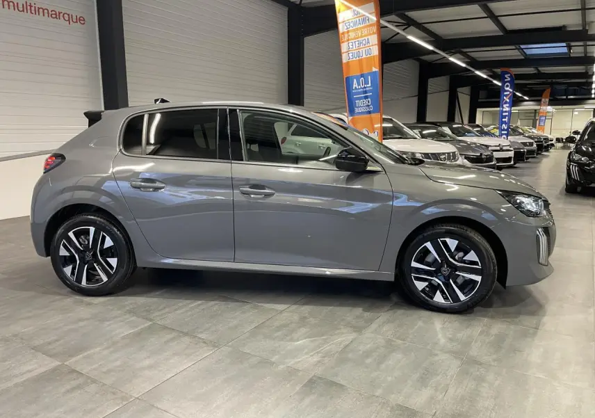 Profil droit d'une Peugeot 208 hybride gris selenium avec jantes alliage bi-ton dans un showroom.