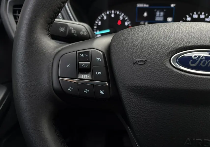 Gros plan sur le volant en cuir noir du Ford Kuga 2024 avec commandes multifonctions et logo Ford central.