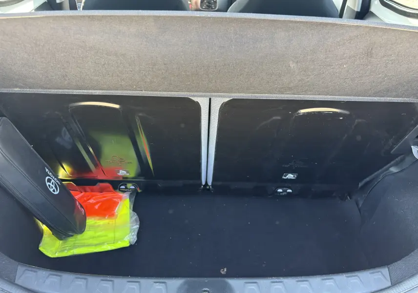 Vue du coffre ouvert d'une Toyota Aygo MC blanche 2020, avec un gilet de sécurité et une trousse de secours visibles.