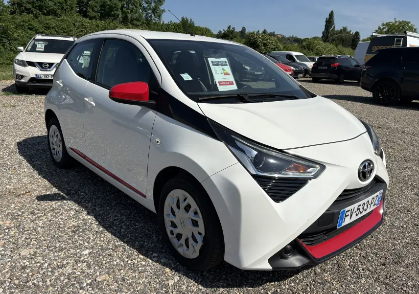 Toyota Aygo MC blanc vue 3/4 avant droit avec rétroviseurs rouges et détails rouges sur pare-chocs et bas de porte.