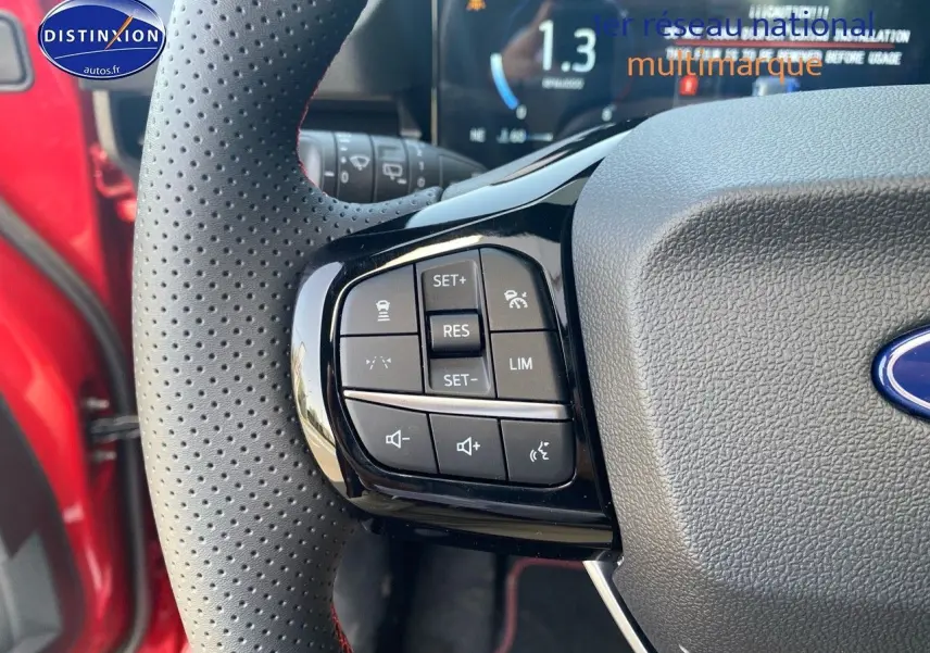 Gros plan sur les commandes multifonctions du volant perforé côté gauche d’un Ford Puma rouge métallisé.