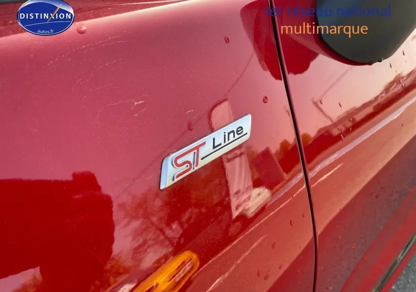Gros plan sur l’écusson ST-Line côté gauche d’un Ford Puma rouge métallisé avec reflet et gouttes d’eau.