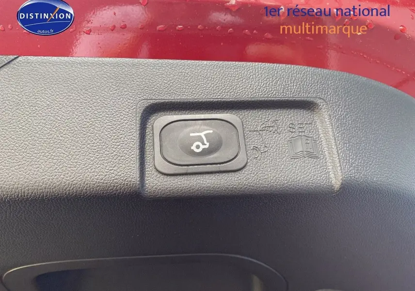 Gros plan sur le bouton d'ouverture électrique du coffre, entouré de plastique noir, sur une Ford Puma rouge.