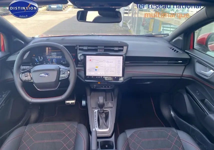 Vue intérieure avant du Ford Puma rouge, montrant le volant multifonction, l’écran tactile central et les sièges sport avec surpiqûres rouges.