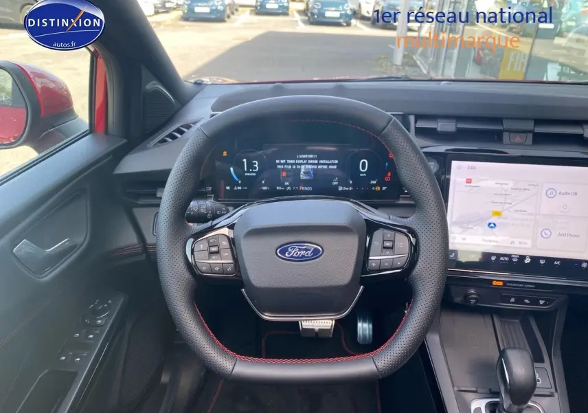 Vue intérieure centrée sur le volant perforé avec surpiqûres rouges et tableau de bord numérique de la Ford Puma rouge.