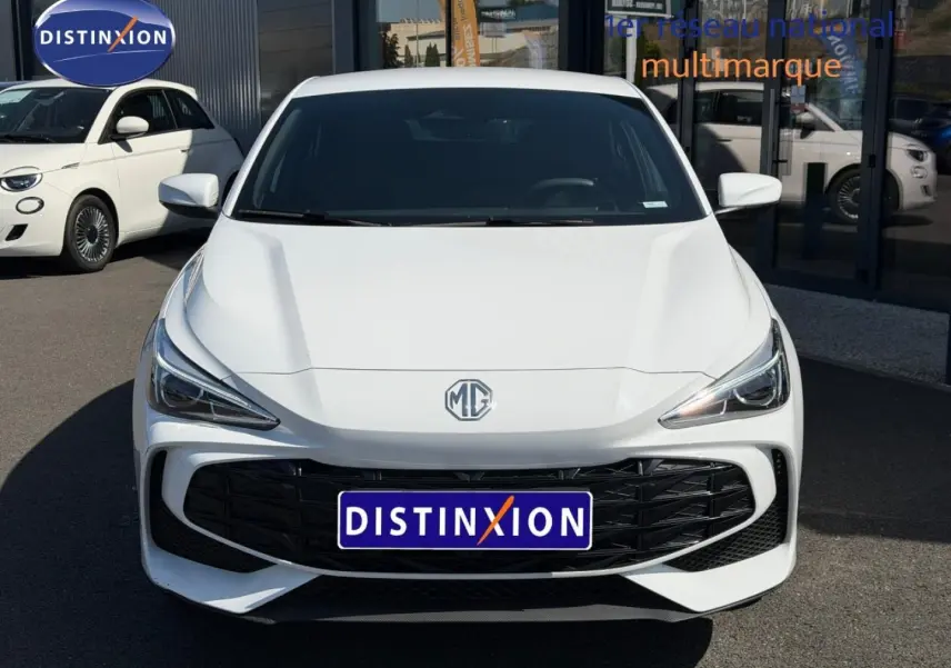 Vue avant d'une MG3 1.5 Hybrid+ blanche avec calandre noire et phares LED, stationnée devant un bâtiment commercial.