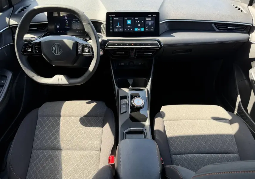 Vue intérieure avant du MG3 1.5 Hybrid+ 195ch Comfort 2025, avec tableau de bord numérique et sièges tissu gris à motifs.