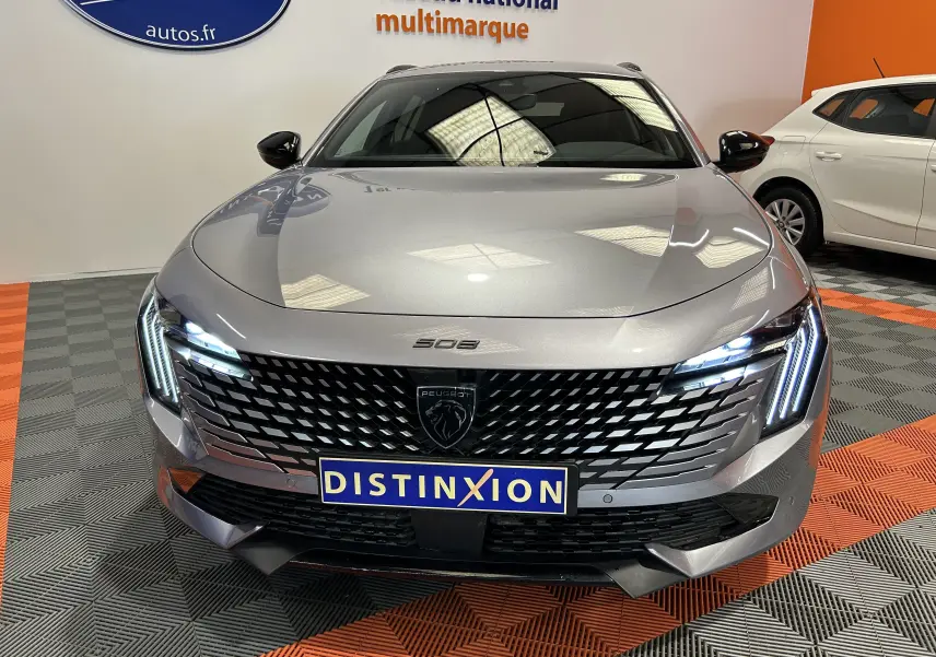 Vue avant d'une Peugeot 508 SW BlueHDi 130 GT gris artense avec calandre noire et phares LED allumés en intérieur showroom.