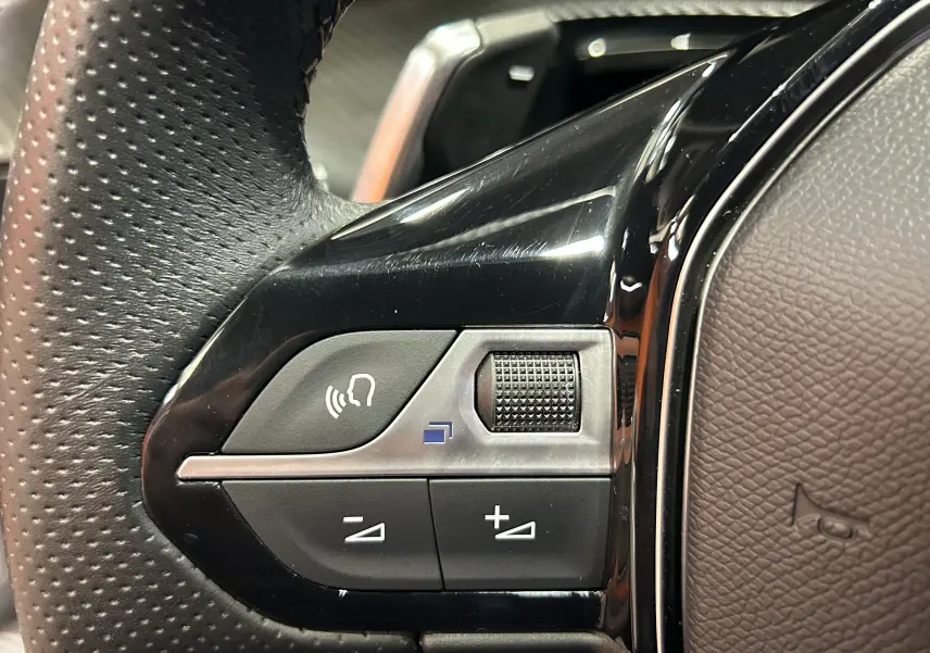Gros plan sur les commandes noires et argentées du volant perforé d'une Peugeot 508 SW Gris Artense 2024.