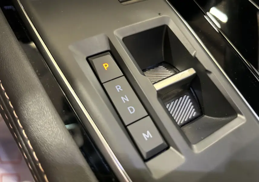 Gros plan sur la commande de boîte automatique noire avec boutons P, R, N, D, M dans un Peugeot 508 SW 2024 gris artense.