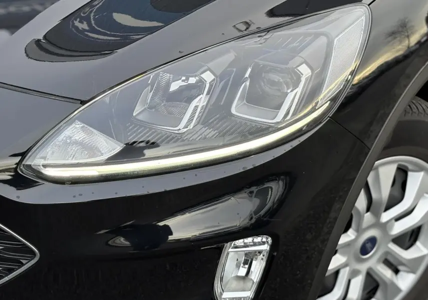 Gros plan sur le phare avant droit du Ford Kuga noir Obsidien 2024 avec jante alliage visible.