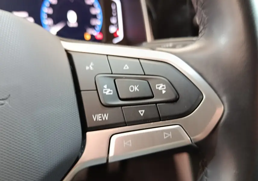 Gros plan sur les commandes multifonctions du volant cuir alu du Volkswagen Taigo gris foncé, tableau de bord numérique en arrière-plan.