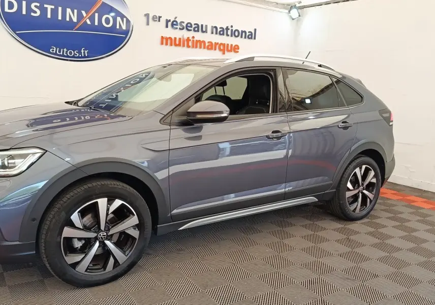 Vue de profil côté gauche du Volkswagen Taigo gris foncé avec jantes alliage et barres de toit chromées en intérieur showroom.