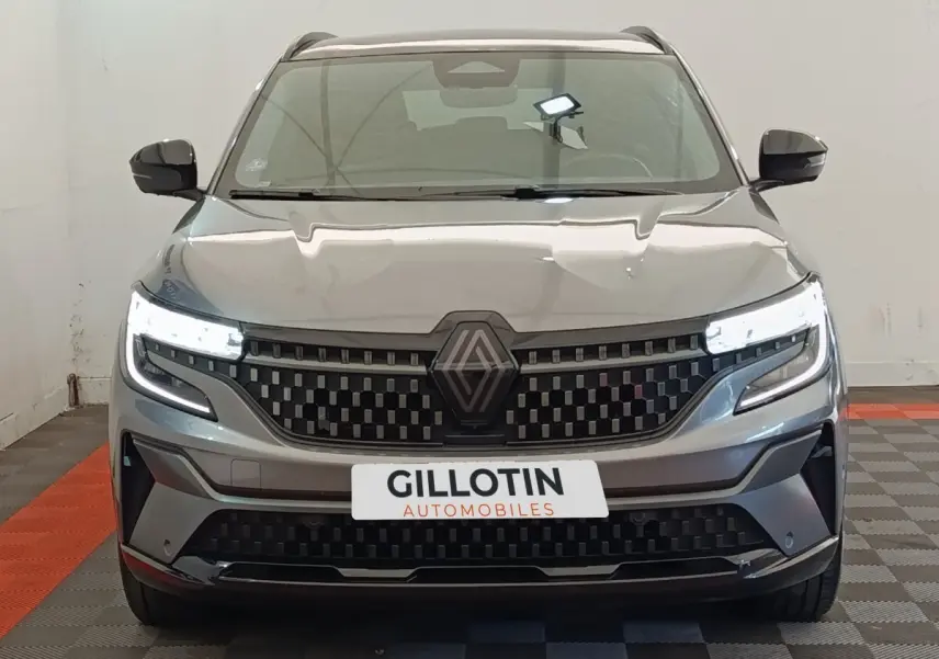 Vue frontale du Renault Austral gris clair avec calandre à damier et phares LED allumés dans un showroom.