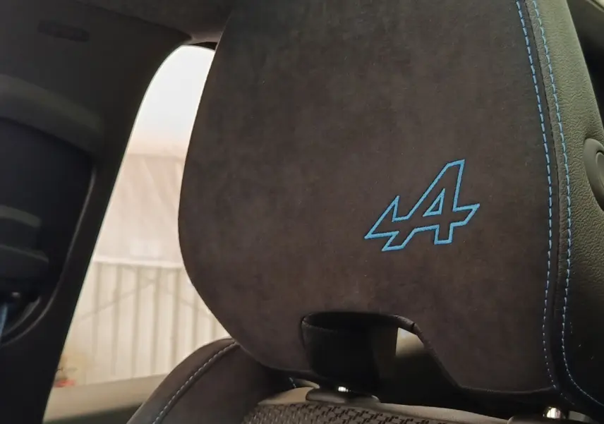 Gros plan sur l’appui-tête arrière en suédine noire avec logo Alpine bleu et surpiqûres assorties.