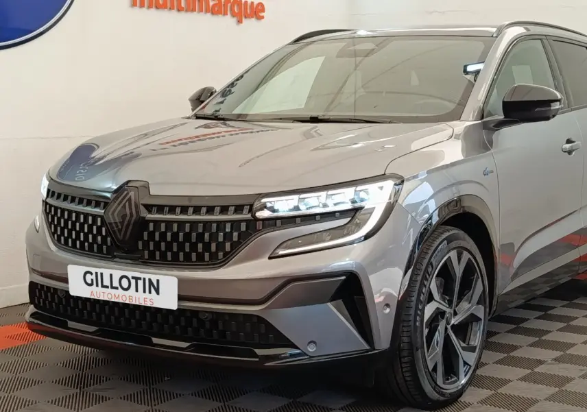 Vue 3/4 avant droite du Renault Austral gris clair avec calandre noire et phares LED allumés en intérieur showroom.