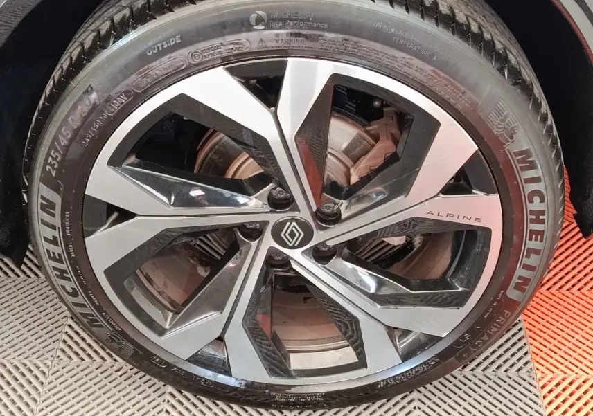 Gros plan sur la jante aluminium bicolore avec logo Renault et inscription Alpine sur un Renault Austral gris clair.