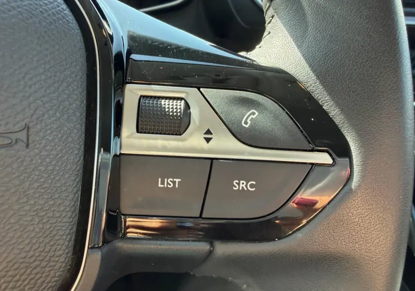 Gros plan sur les commandes audio au volant noir brillant de la Peugeot 208 gris Artense, version 2025.