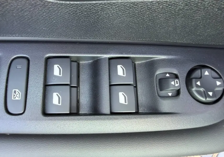 Gros plan sur les commandes des vitres et rétroviseurs côté gauche d'une Peugeot 208 gris Artense 2025.